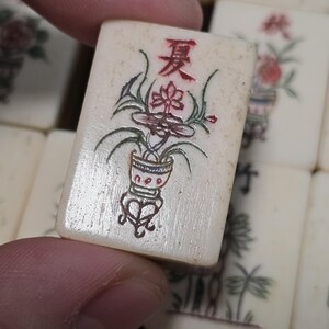 Puede incluir: Una ficha de Mahjong rectangular de color blanco hueso con el car&aacute;cter chino rojo para verano en la parte superior, sobre una ilustraci&oacute;n detallada de una planta en maceta con hojas verdes y detalles rojos, entre otras fichas.