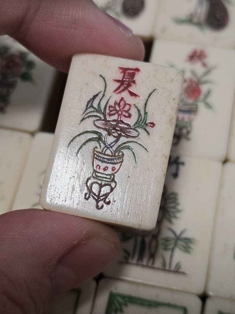 Puede incluir: Una ficha de Mahjong rectangular de color blanco hueso con el car&aacute;cter chino rojo para verano en la parte superior, sobre una ilustraci&oacute;n detallada de una planta en maceta con hojas verdes y detalles rojos, entre otras fichas.