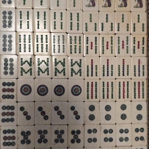 May include: A set of off-white Mahjong tiles arranged in a grid, featuring engraved symbols including green bamboo sticks, circular patterns, and bird illustrations. The tiles display various numerical and suit markings in green, red, and blue ink.