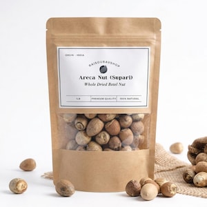 May include: A brown paper bag with a clear window displays whole dried betel nuts, labeled as Areca Nut (Supari). A small burlap sack and loose nuts are also visible, with the text "1 LB" on the label.