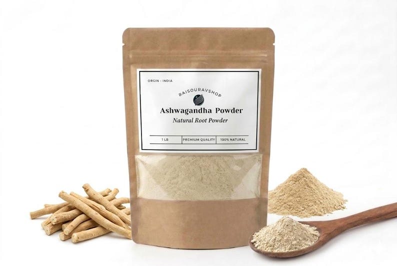 May include: A brown paper bag of Ashwagandha Powder with a clear window, a pile of powder, and a wooden spoon. The bag has a white label with text. Ashwagandha root sticks are to the left.