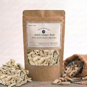Op de afbeelding: Een bruine papieren zak met een doorzichtig venster met gedroogde gemberwortel. Het etiket luidt "Dried Ginger Root Whole Sonth (Zingiber Officinale)". Een stapel gedroogde gemberwortel ligt ervoor, met een jute zak en een schep rechts.