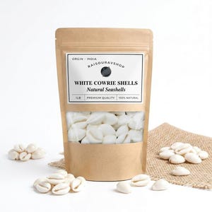 May include: A brown paper pouch containing white cowrie shells with a label reading ORGIN INDIA RAISOURAVSHOP WHITE COWRIE SHELLS Natural Seashells 1LB PREMIUM QUALITY 100% NATURAL. Several loose white cowrie shells are scattered around the base.
