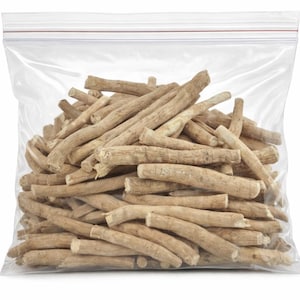 May include: A transparent plastic bag containing a large quantity of light brown, dried ashwagandha root pieces. The roots are cylindrical and have a rough texture. The bag has a zip-top closure. The background is plain white.