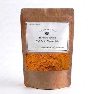 Op de afbeelding: Een bruine stazak met 454g feloranje kurkumapoeder. Het witte etiket bevat de tekst: ORGIN - INDIA, RAI SOURAV SHOP, Turmeric Powder, High Purity Natural Spice, 1 LB, PREMIUM QUALITY, 100% NATURAL. Een doorzichtig venster toont het poeder.