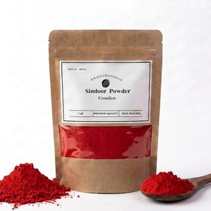 May include: A brown paper bag of Sindoor Powder, labeled "Vermilion," with a clear window showing the red powder. A pile of red powder and a wooden spoon with red powder are next to the bag. The bag is labeled "1 LB."