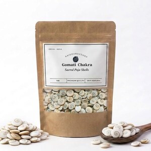 Pode incluir: Um saco de papel castanho com uma janela transparente cheia de conchas Gomati Chakra Sacred Puja. Uma colher de pau e uma pilha de conchas estão ao lado do saco. O rótulo diz "RAISOURAVSHOP" e "100% NATURAL".