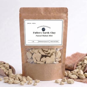 May include: A brown paper bag with a clear window containing Fuller's Earth Clay. The bag has a white label with text. Two wooden scoops and scattered clay pieces are on either side. The text on the label reads "Fuller's Earth Clay, Natural Multani Mitti."