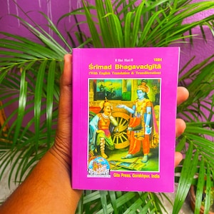 Peut inclure: Un livre rose intitulé "Śrīmad Bhagavadgītā" avec traduction et translittération anglaises. La couverture présente une illustration de deux personnages et un char. Publié par Gita Press, Gorakhpur, Inde.