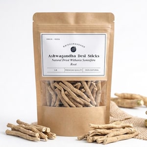 Peut inclure: Un sac en papier brun avec une fenêtre transparente montrant des bâtonnets de desi ashwagandha. L'étiquette indique "Ashwagandha Desi Sticks Natural Dried Withania Somnifera Root". Plusieurs bâtonnets sont éparpillés autour du sac.