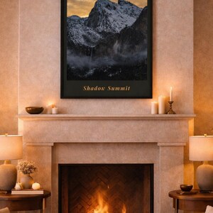 Puede incluir: Una impresión enmarcada titulada "Shadow Summit" representa una cordillera nevada bajo un cielo dorado. La impresión cuelga sobre una chimenea con fuego, flanqueada por lámparas y mesas auxiliares.