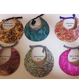 Könnte beinhalten: Sechs Sonnenblenden mit Batikmustern in Braun/Beige, Blaugrün/Grün, Pink, Abendrot, Blau/Gold und Beerenrosa. Jede Blende hat einen geschwungenen Schirm und ein spiralförmiges elastisches Band zur Anpassung, mit Textbeschriftungen für jede Farbvariante.