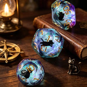 May include: Three multi-faceted, iridescent dice with gold numbers and black cat silhouettes. The dice are on a wooden surface with a small cat figurine, a compass, a book, and a lit lantern in the background. The dice are a fantasy gaming accessory.