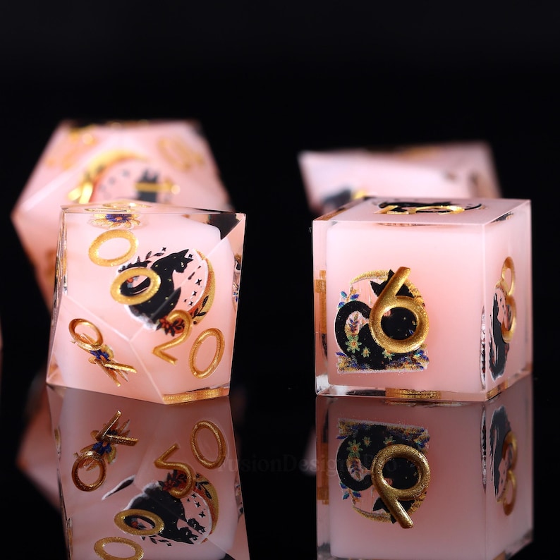 Pode incluir: Dados rosa e dourados com ilustra&ccedil;&otilde;es pretas e douradas. Os dados t&ecirc;m n&uacute;meros e s&iacute;mbolos dourados. Os dados est&atilde;o sobre uma superf&iacute;cie refletora.