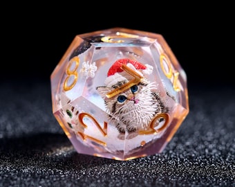 May include: A clear, multi-sided die with gold numbering and a festive kitten wearing a Santa hat inside. The kitten has blue eyes and is surrounded by a snowy scene. The die is a unique item for tabletop gaming.