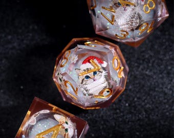 Könnte beinhalten: Drei polyedrische Würfel mit eingebetteten Katzenillustrationen. Jeder Würfel zeigt eine andere goldene Zahl und ein detailliertes Bild eines Kätzchens mit Weihnachtsmütze. Die Würfel sind transparent mit glitzerndem Hintergrund.
