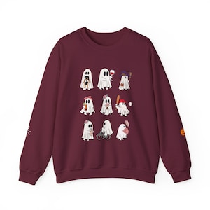 Op de afbeelding: Een bordeauxrode sweatshirt met een verzameling cartoongeesten, elk met unieke accessoires. Sommige geesten houden voorwerpen vast zoals wijnglazen, honkbalknuppels en bloemen. De mouwen hebben kleine Halloween-thema graphics. Een leuk, feestelijk ontwerp voor het griezelige seizoen.