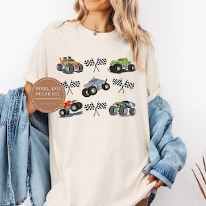 May include: Cream-colored t-shirt featuring colorful monster trucks and checkered flags. The graphic includes orange, green, red, purple, and gray monster trucks. The text "PIXEL AND PULSE CO. ESTD 2020" is printed on a circular label.