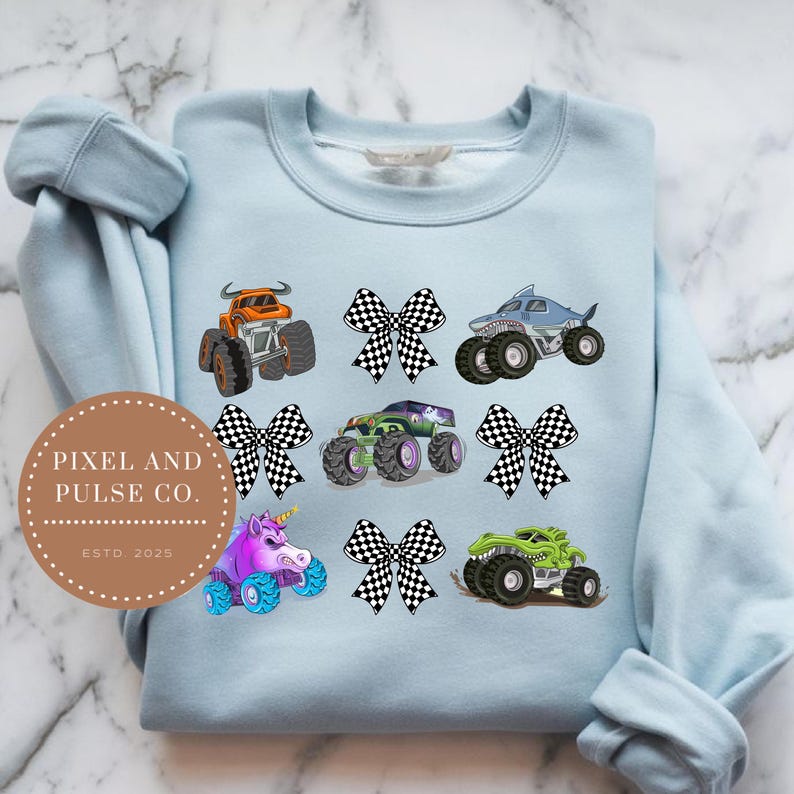 K&ouml;nnte beinhalten: Hellblaues Sweatshirt mit bunten Monstertruck-Designs, darunter ein Hai, ein Einhorn und ein Stier. Das Design enth&auml;lt auch karierte Schleifen. Das Sweatshirt hat den Text "PIXEL AND PULSE CO. ESTD. 2025" in einem kreisf&ouml;rmigen Logo.