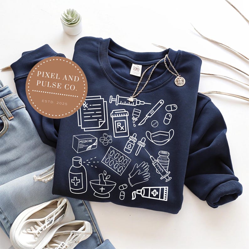 Puede incluir: Sudadera azul marino con ilustraciones m&eacute;dicas blancas, incluyendo jeringas, pastillas y s&iacute;mbolos de receta. La sudadera se combina con vaqueros azules y zapatillas blancas. Se ve un collar con un colgante.