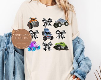 Könnte beinhalten: Cremefarbenes T-Shirt mit farbenfrohen Monster-Truck-Grafiken und karierten Schleifen. Das Design umfasst einen orangefarbenen Truck, einen Truck im Hai-Design, einen blauen Truck mit Monstergesicht, einen lila Einhorn-Truck und einen grünen Truck. Das Shirt hat den Text "PIXEL AND PULSE CO. ESTD. 2020".