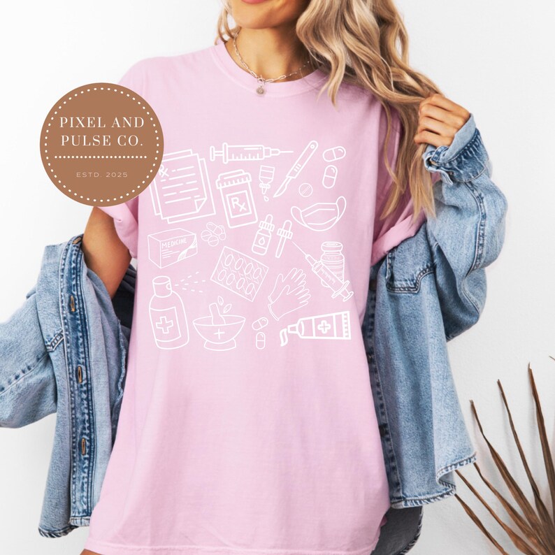 Puede incluir: Camiseta rosa claro con un dise&ntilde;o blanco de contorno de suministros m&eacute;dicos, incluyendo jeringas y pastillas. La camiseta tambi&eacute;n tiene el texto "PIXEL AND PULSE CO. ESTD. 2025" en un logotipo circular.