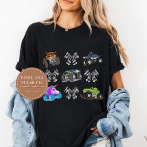 May include: Black t-shirt featuring colorful monster truck designs and checkered bows. The shirt includes an orange, blue, green, and purple monster truck, along with a unicorn monster truck. The shirt also has the text "Pixel and Pulse Co. Estd. 2025".