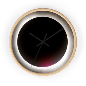 Puede incluir: Un reloj de pared redondo con una imagen en blanco y negro de un eclipse solar. Las manecillas del reloj son negras y la esfera está rodeada por un marco de madera clara.