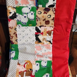 May include: A patchwork quilt featuring squares with farm animal patterns, including pigs, sheep, cows, and rabbits. The quilt has a red border and is displayed over a wooden surface. The quilt is a mix of colors, including green, white, pink, and brown.