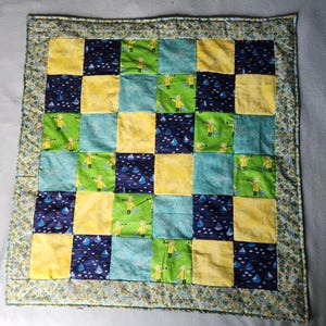 May include: A patchwork quilt with a green, yellow, and blue color scheme. The quilt is made up of squares with different patterns, including a pattern of a boy in a yellow raincoat.