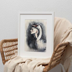 May include: A framed art print featuring a watercolor illustration of a person in profile with a white swan draped over their head. The swan has a black beak with a red patch. The background is a smoky, dark gray wash, all encased in a white frame.