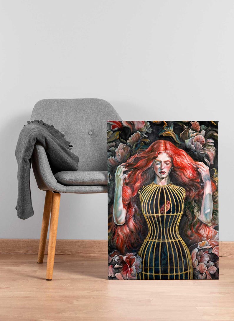 Op de afbeelding: Een rechthoekige canvasprint met een schilderij van een persoon met lang, golvend rood haar. De persoon draagt een goudkleurig kooivormig lijfje over een donker kledingstuk. Een kleine rode vogel zit in de kooi. De achtergrond bestaat uit donkere bloemen.