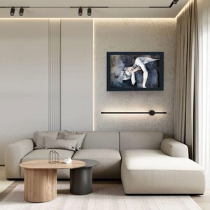 May include: A rectangular framed wall art piece featuring a monochromatic illustration of a reclining figure in shades of black, gray, and white. The artwork is displayed on a textured wall above a beige sectional sofa and two round coffee tables.