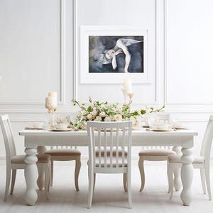 May include: A white dining table with four matching chairs, a large white floor vase filled with white branches, and a framed rectangular art print featuring a figure in a dark, moody setting hanging on the wall above the table.