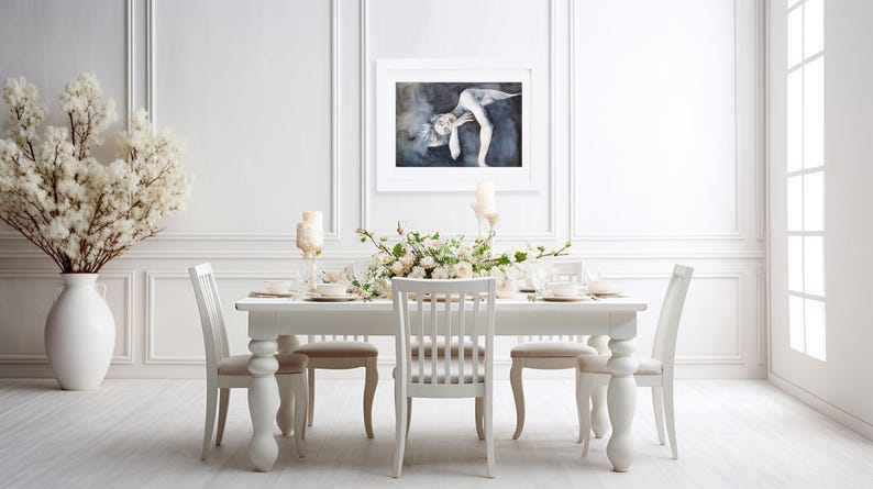 May include: A white dining table with four matching chairs, a large white floor vase filled with white branches, and a framed rectangular art print featuring a figure in a dark, moody setting hanging on the wall above the table.