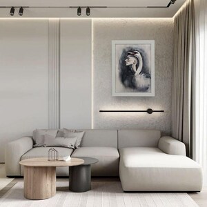 May include: A light gray sectional sofa with a chaise lounge, two round coffee tables in wood and dark gray, and a framed wall art piece depicting a person with a swan head. The room features neutral walls, beige curtains, and a textured rug.