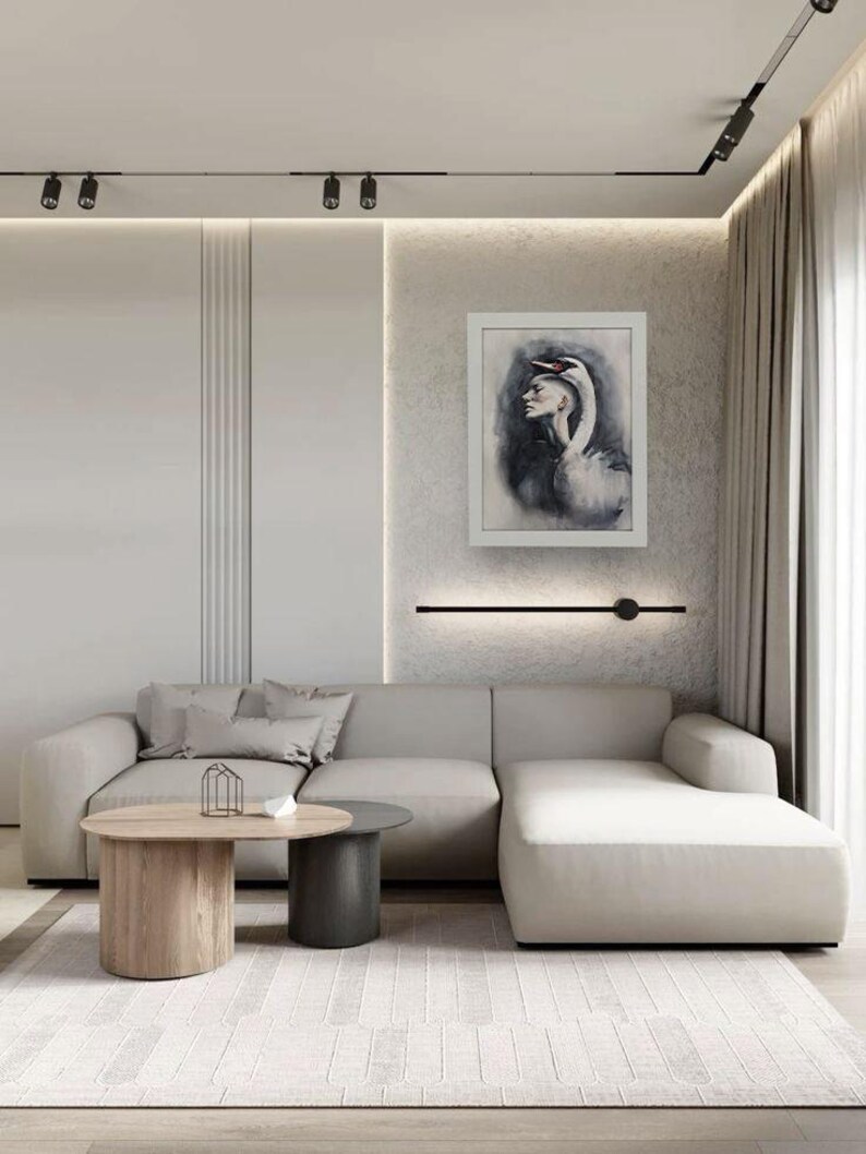May include: A light gray sectional sofa with a chaise lounge, two round coffee tables in wood and dark gray, and a framed wall art piece depicting a person with a swan head. The room features neutral walls, beige curtains, and a textured rug.