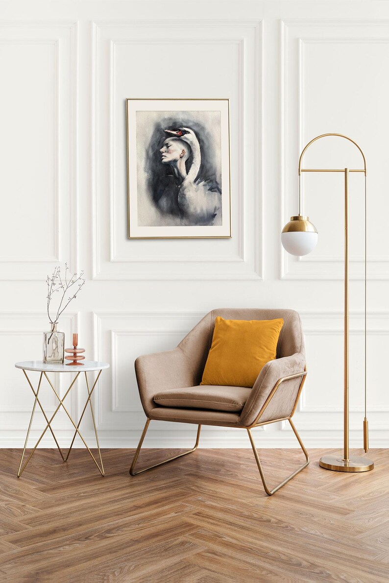May include: A framed wall art print featuring a surreal illustration of a person with a swan head, displayed in a room with a beige armchair, a mustard yellow pillow, a white side table, and a tall gold floor lamp with a white globe shade.