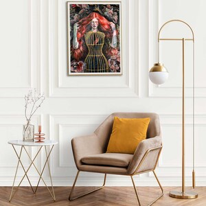 Op de afbeelding: Een ingelijste kunstdruk met een schilderij van een persoon met lang rood haar die een goudkleurig kooivormig lijfje draagt, omringd door donkere florale elementen. Het kunstwerk staat in een kamer met een beige fauteuil, een gouden vloerlamp en een tafeltje.