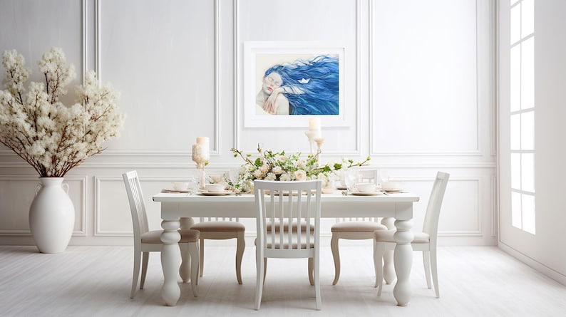 May include: A framed rectangular wall art print featuring a portrait of a person with long, flowing blue hair and closed eyes, with a small white paper boat resting in the hair, displayed in a white frame on a white paneled wall above a dining table.