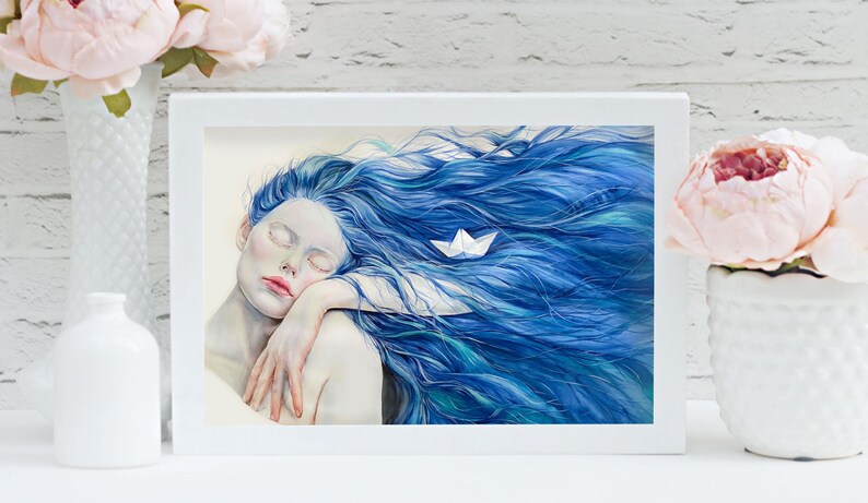 May include: A framed art print featuring a painting of a person with pale skin and long, flowing blue hair. A small white paper boat rests within the hair. The person has their eyes closed and is resting their head on their arm in a calm pose.