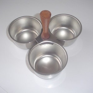 May include: A silver three-compartment serving dish with a wooden handle. The dish is ideal for serving snacks, dips, or condiments.