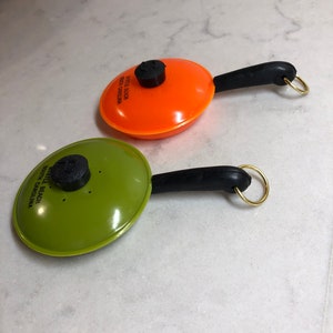 May include: Two small orange and green plastic frying pan keychains with black handles and gold rings. The orange pan has the text "Myrtle Beach South Carolina" printed on it. The green pan has the text "Myrtle Beach South Carolina" printed on it.