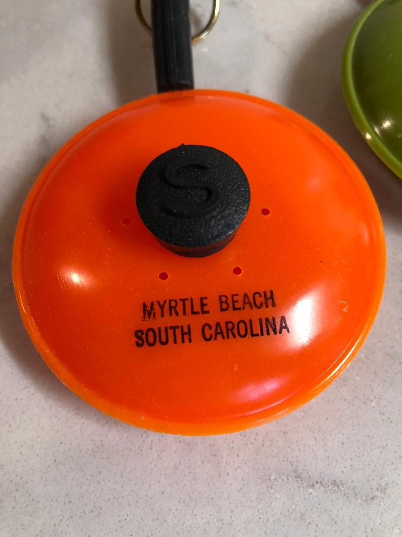 May include: Orange plastic frying pan keychain with a black knob and the text "Myrtle Beach South Carolina".
