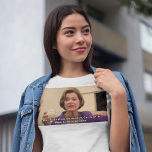 Puede incluir: Camiseta blanca con una imagen de una mujer sosteniendo una copa de vino. El texto en la camiseta dice "Well, I'd rather be dead in California than alive in Arizona."