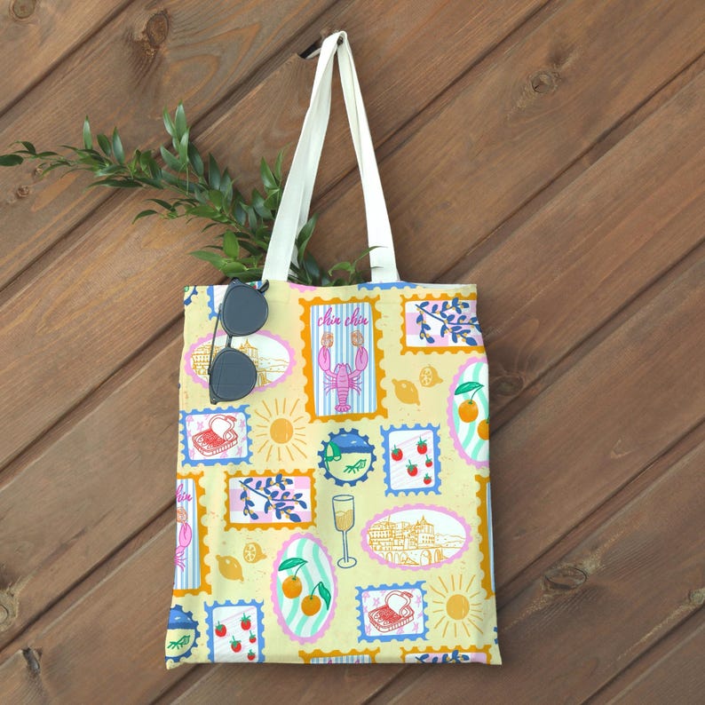 Pu&ograve; includere: Una borsa tote giallo chiaro con un motivo ripetuto di disegni di francobolli con un'aragosta, un sole e frutta. La borsa ha manici bianchi ed &egrave; appesa su uno sfondo di legno. Gli occhiali da sole sono attaccati alla borsa.