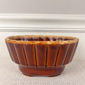 May include: A brown glazed ceramic bowl with a fluted design. The bowl has a light brown glaze on the top edge and a darker brown glaze on the bottom.