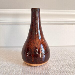 May include: A small, brown ceramic vase with a teardrop shape and a speckled glaze.