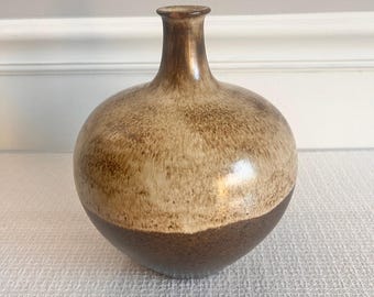 May include: A brown and cream ceramic vase with a rounded body and a narrow neck. The vase has a mottled glaze and a dark brown base.