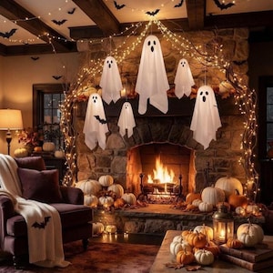 May include: A Halloween fireplace display featuring white ghost decorations hanging from branches wrapped in warm string lights. The stone hearth is decorated with numerous orange pumpkins, a metal lantern, and black bat silhouettes.